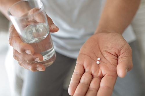 Close up of senior Caucasian man sitting on the bed while holding pills and a glass of water. Authentic Senior Retired Life Concept