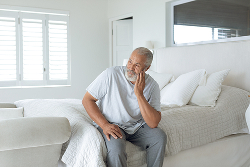 Side view of thoughtful senior Caucasian man sitting on the bed in bedroom. Authentic Senior Retired Life Concept