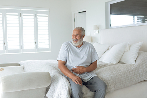 Side view of senior Caucasian man smiling and sitting on the bed in bedroom. Authentic Senior Retired Life Concept