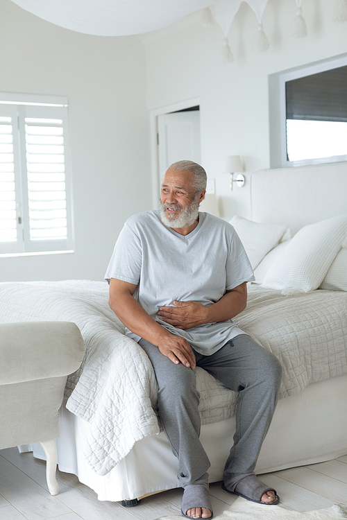 Side view of senior Caucasian man smiling and sitting on the bed in bedroom. Authentic Senior Retired Life Concept