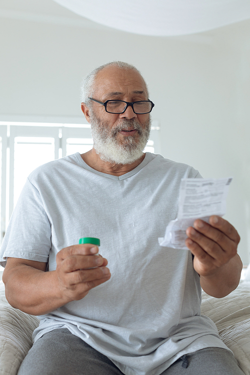 Front view of senior Caucasian man sitting on the bed while reading through the prescription. Authentic Senior Retired Life Concept