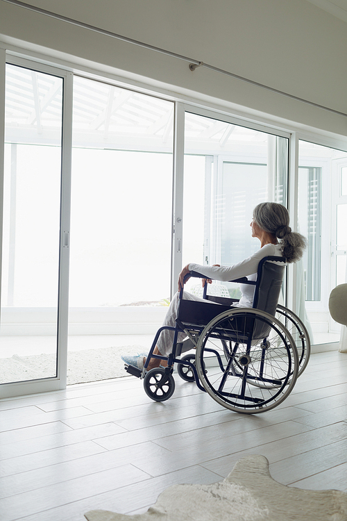 Side view of woman on wheelchair looking outside indoor. Authentic Senior Retired Life Concept