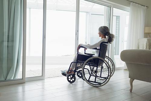 Side view of woman on wheelchair looking outside indoor. Authentic Senior Retired Life Concept