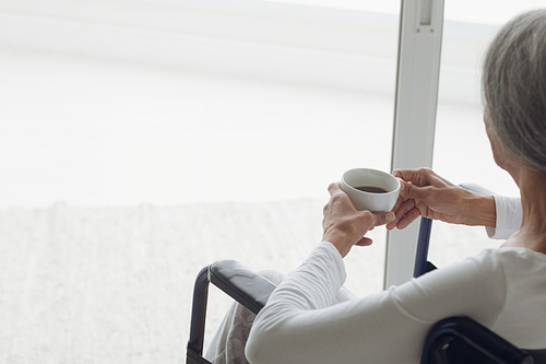 Rear view close up of woman on wheelchair drinking coffee indoor. Authentic Senior Retired Life Concept