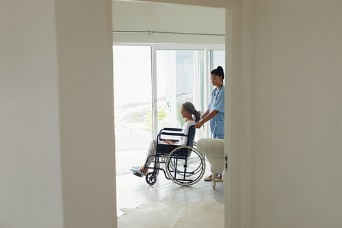 Side view of healthcare worker and woman on a wheelchair indoor. Authentic Senior Retired Life Concept