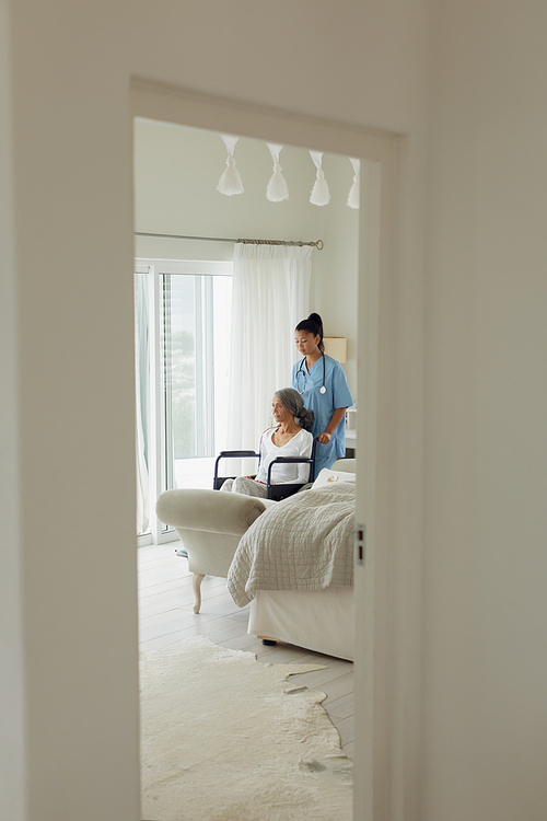 Side view of healthcare worker and woman on a wheelchair indoor. Authentic Senior Retired Life Concept