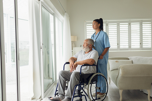 Side view of healthcare worker and man on wheelchair indoor. Authentic Senior Retired Life Concept