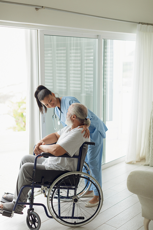 Side view of healthcare worker talking with man on wheelchair indoor. Authentic Senior Retired Life Concept