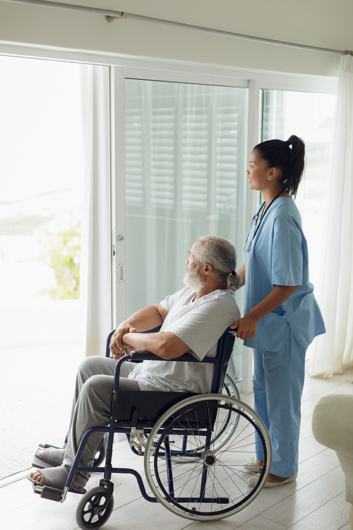 Side view of healthcare worker with man on wheelchair indoor. Authentic Senior Retired Life Concept