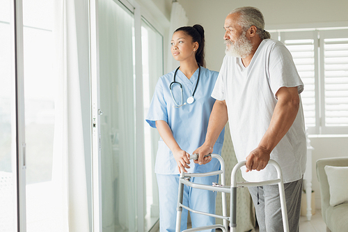 Side view of healthcare worker with man using walking support indoor. Authentic Senior Retired Life Concept