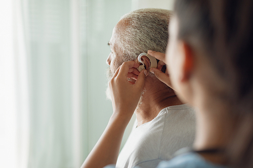 Rear view of healthcare worker putting hearing aid indoor. Authentic Senior Retired Life Concept