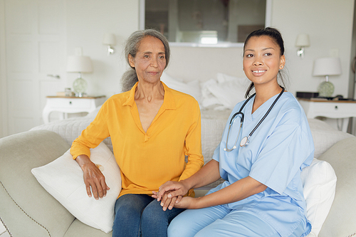 Front view of mixed-race woman healthcare worker and woman sitting on couch indoor. Authentic Senior Retired Life Concept