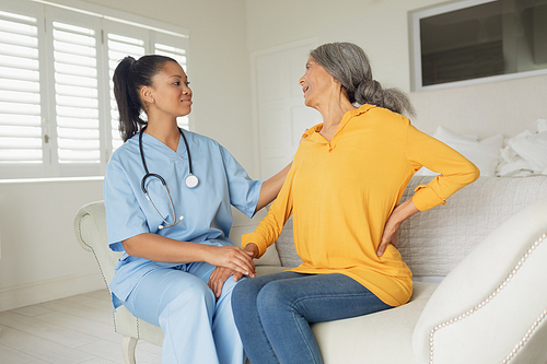 Side view of mixed-race woman healthcare worker and woman sitting on couch indoor. Authentic Senior Retired Life Concept