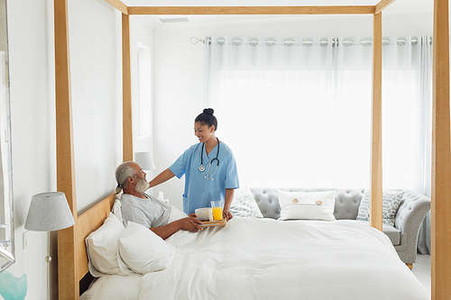 Overview of mixed race healthcare worker talking with old man in bed. Authentic Senior Retired Life Concept