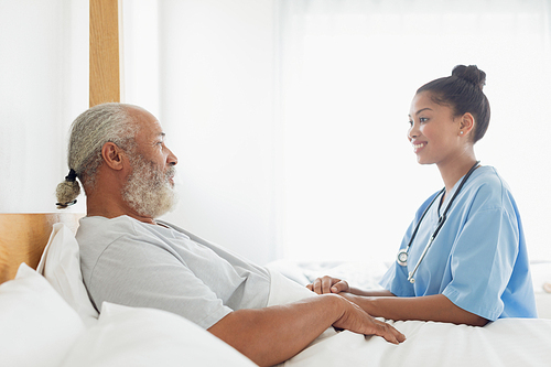 Side view of mixed race healthcare worker talking with old man in bed. Authentic Senior Retired Life Concept