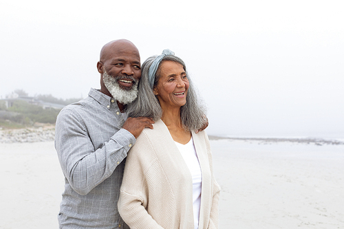 Front view of happy senior African-American couple standing on the beach on cloudy day. Authentic Senior Retired Life Concept