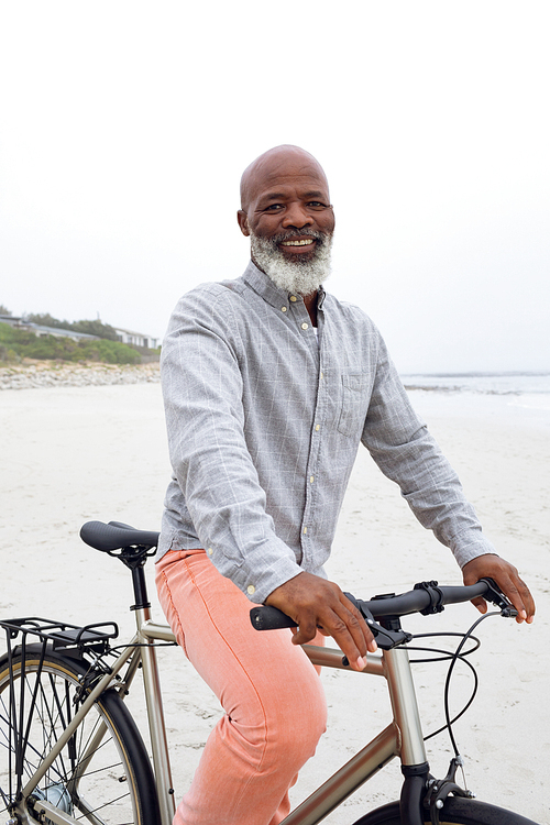 Front view of handsome Senior African-American man with bicycle on beach on cloudy day. Authentic Senior Retired Life Concept