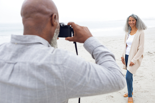 Rear view of African american Man taking a picture of woman at the beach. Authentic Senior Retired Life Concept