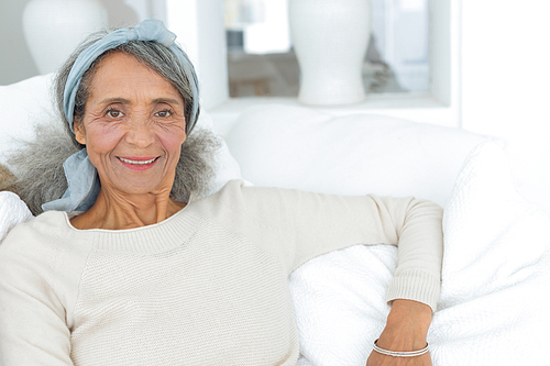 Front view of happy senior mixed race Woman smiling while sitting on white couch. Authentic Senior Retired Life Concept