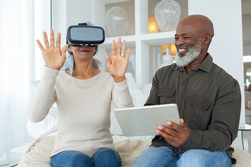 Front view of diverse senior couple using digital devices while sitting inside a room in beach house. Authentic Senior Retired Life Concept