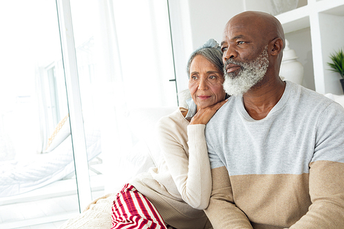 Side view of happy senior diverse couple sitting in a white room while looking away from the camera in beach house. Authentic Senior Retired Life Concept