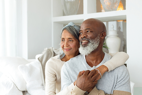 Front view of senior diverse couple sitting on a white couch in beach house. Authentic Senior Retired Life Concept