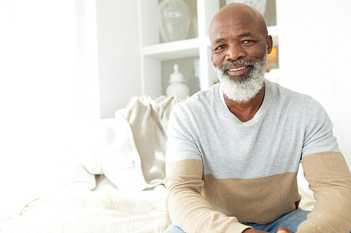 Front view of happy senior African-American man smiling while sitting on white sofa in beach house. Authentic Senior Retired Life Concept
