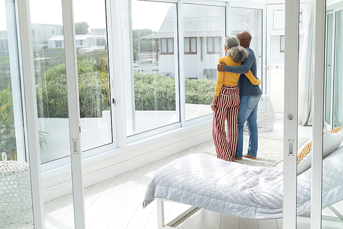 Rear view of African American Couple standing close together while looking out the window. Authentic Senior Retired Life Concept