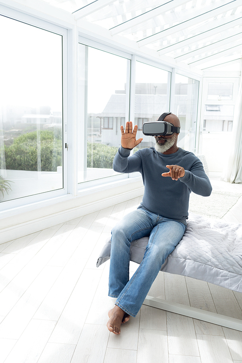 Front view of African American Man sitting on bed while using virtual goggles. Authentic Senior Retired Life Concept