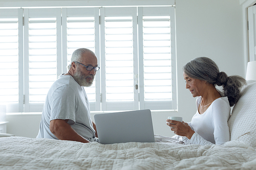 Side view of senior diverse couple sitting on bed inside a room. Authentic Senior Retired Life Concept