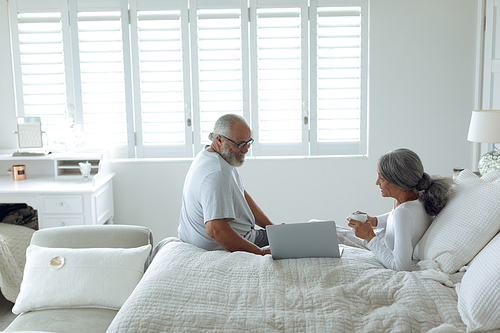 Side view of senior diverse couple sitting on bed inside a room. Authentic Senior Retired Life Concept