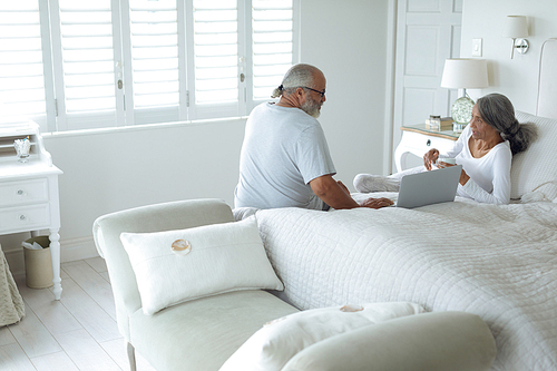 Side view of senior diverse couple sitting on bed inside a room. Authentic Senior Retired Life Concept