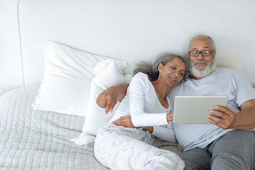 Side view of senior diverse couple lying in bed and watching digital tablet in bedroom. Authentic Senior Retired Life Concept