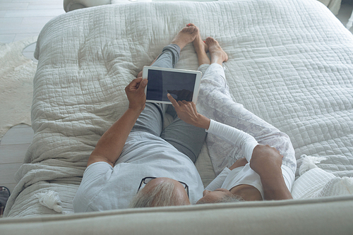 Over the shoulder view of senior diverse couple lying in bed and watching digital tablet in bedroom. Authentic Senior Retired Life Concept