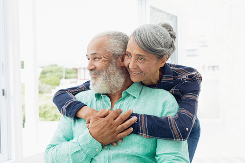 Side view of African-American  couple smiling and hugging each other inside a room. Authentic Senior Retired Life Concept