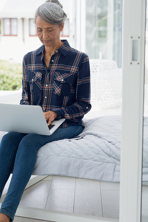 Front view of senior African-American  woman using laptop while sitting on bed in bedroom. Authentic Senior Retired Life Concept