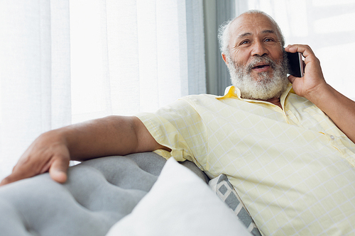 Front view close up of mixed race man talking on mobile phone sitting on a couch. Authentic Senior Retired Life Concept