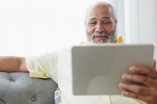 Front view of mixed race man using digital tablet sitting on a couch. Authentic Senior Retired Life Concept
