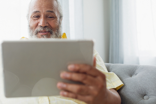 Front view of mixed race man using digital tablet sitting on a couch. Authentic Senior Retired Life Concept