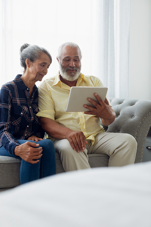 Side view of African-American  couple sitting on a couch while using digital tablet. Authentic Senior Retired Life Concept