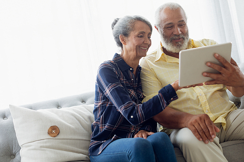 Side view of African-American couple sitting on a couch while using digital tablet. Authentic Senior Retired Life Concept