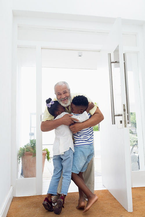 Front view of African american children hugging their grandfather in the hall at home. Authentic Senior Retired Life Concept