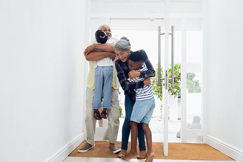 Front view of African american children hugging their grandfather and grandmother in the hall at home. Authentic Senior Retired Life Concept