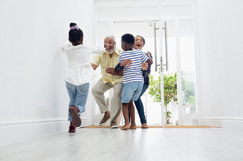 Front view of African american children hugging their grandfather and grandmother in the hall at home. Authentic Senior Retired Life Concept