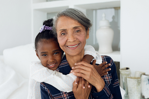 Portrait close up of African american girl and mixed race grandmother sitting on bed. Authentic Senior Retired Life Concept