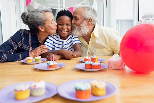 Front view of senior African-American man and woman kissing their grandson for his birthday party. Authentic Senior Retired Life Concept