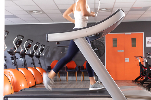 Side view of a Caucasian athletic woman exercising using treadmill inside a room at a sports center. Athlete testing themselves with cardiovascular fitness test on exercise bike