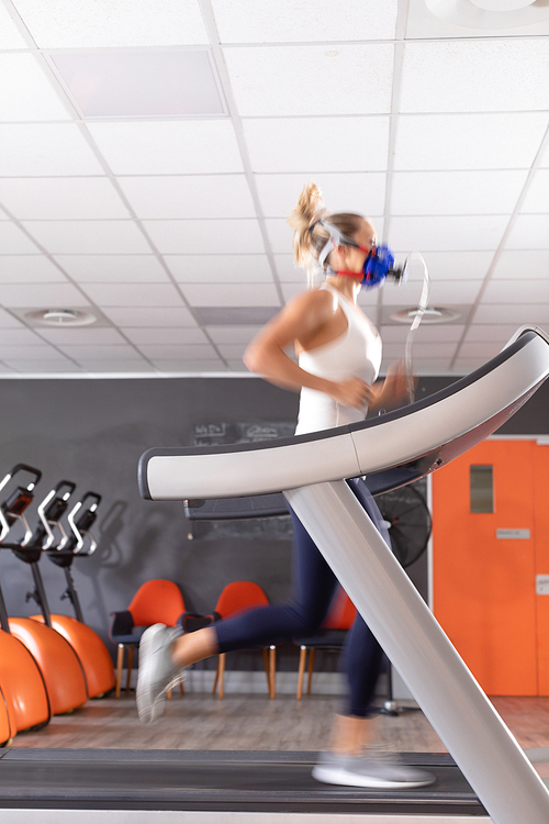 Side view of a Caucasian athletic woman doing a fitness test using a mask while using a treadmill inside a room at a sports center. Athlete testing themselves with cardiovascular fitness test on exercise bike
