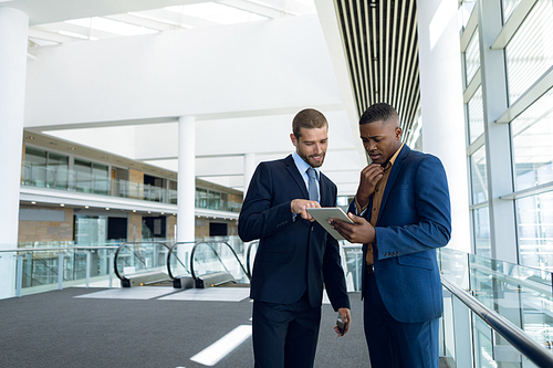 Front view of two young businessmen using tablet together at work standing in the lobby of a modern business building. Modern corporate start up new business concept with entrepreneur working hard