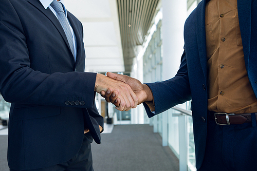 Close up mid-section of two young businessmen shaking hands standing in a modern business building. Modern corporate start up new business concept with entrepreneur working hard